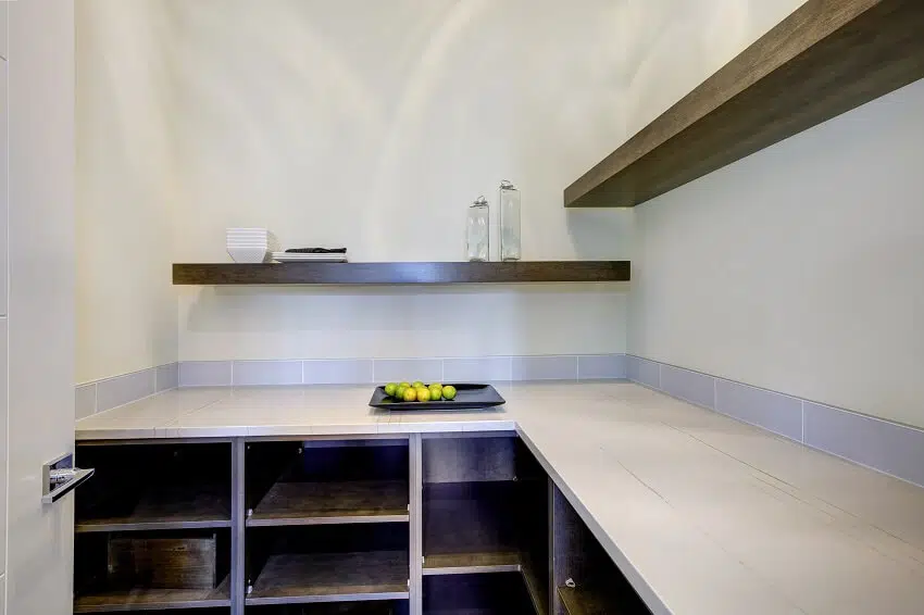 Modern kitchen interior with white cabinets organised pantry items stainless steel counter top brick tile backsplash and kitchen hanging rods with hooks Walk-in pantry with built in empty pantry shelves and open wood shelves on top