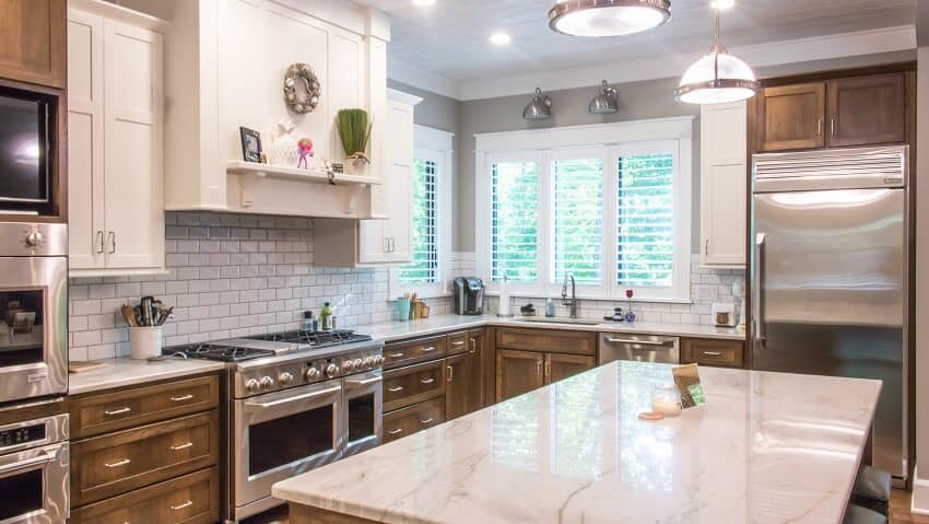 White and brown kitchen with honed marble countertops, stainless steel appliances, and white brick backsplash 