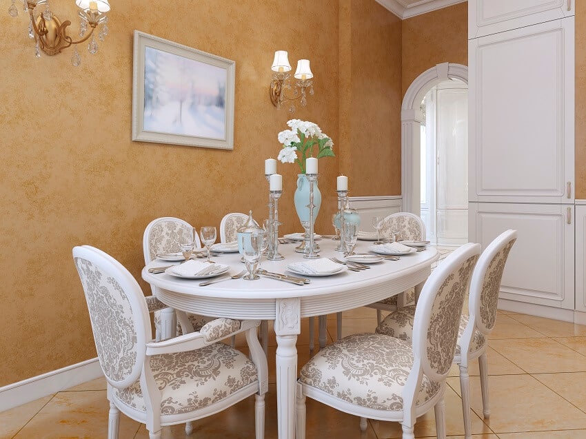 White dining table with chairs in a classic style tile floors wall sconce lighting and orange walls with venetian plaster