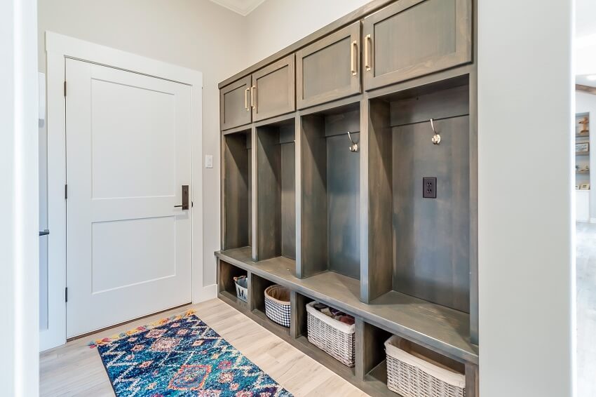 White door and an entryway wooden mudroom with four coat hooks baskets in cubbyholes and rug