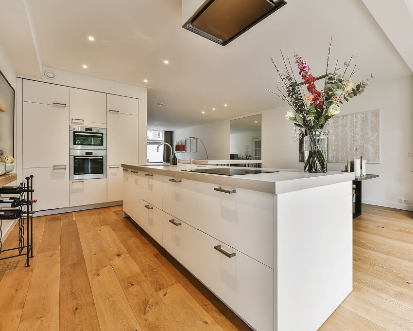 White kitchen island with cooktop sink and flowers in a modern kitchen with wine rack hardwood floors and white walls and ceiling