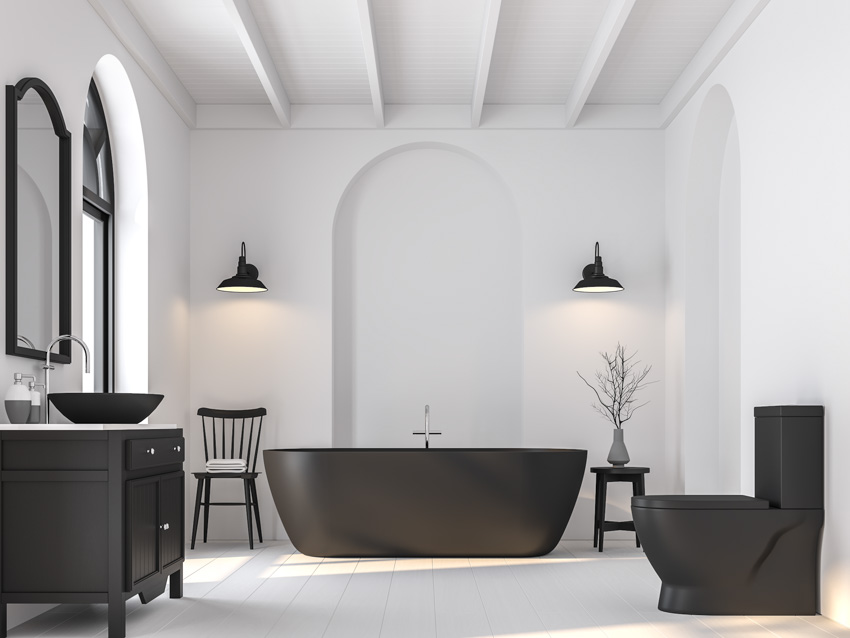 White wall bathroom with black sconces, toilet, vanity, mirror and tub