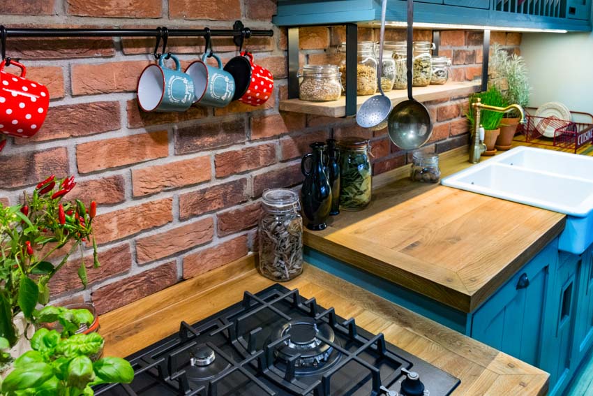 Wood overlay counter, brick backsplash, stove and blue kitchen cabinets