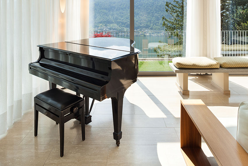 Black piano, curtains, wood bence and view of lake