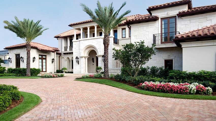 A beautiful white stone estate with red tile roof arch and columns entrance beautiful landscapes and brick pavers