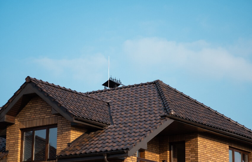 A brick house with dark brown tile roof and a lightning rod