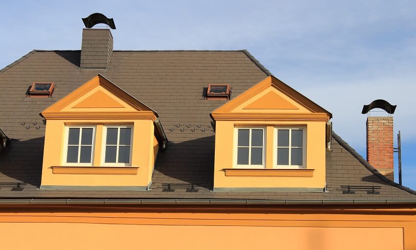 A brown asphalt shingles roof with two bricks chimneys with metal caps two roof hatches and two dormers in a neoclassical style with orange facade