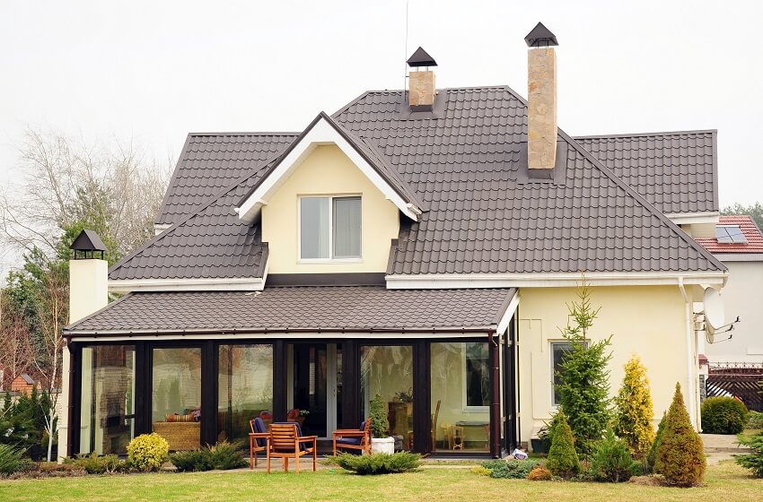 A house with chimneys brown roof yellow exterior paint lightning rod and a garden with armchairs