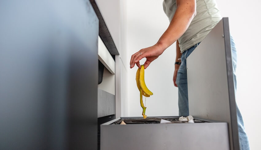 A man throwing a banana peel to a trash compactor