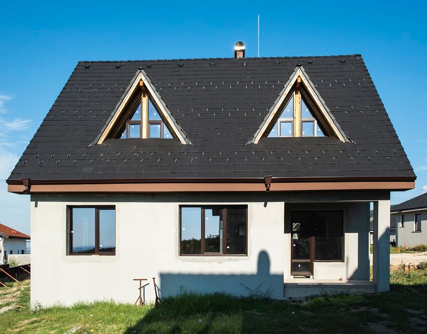 A newly constructed house with attic windows lightning rod black roof and a porch with a column