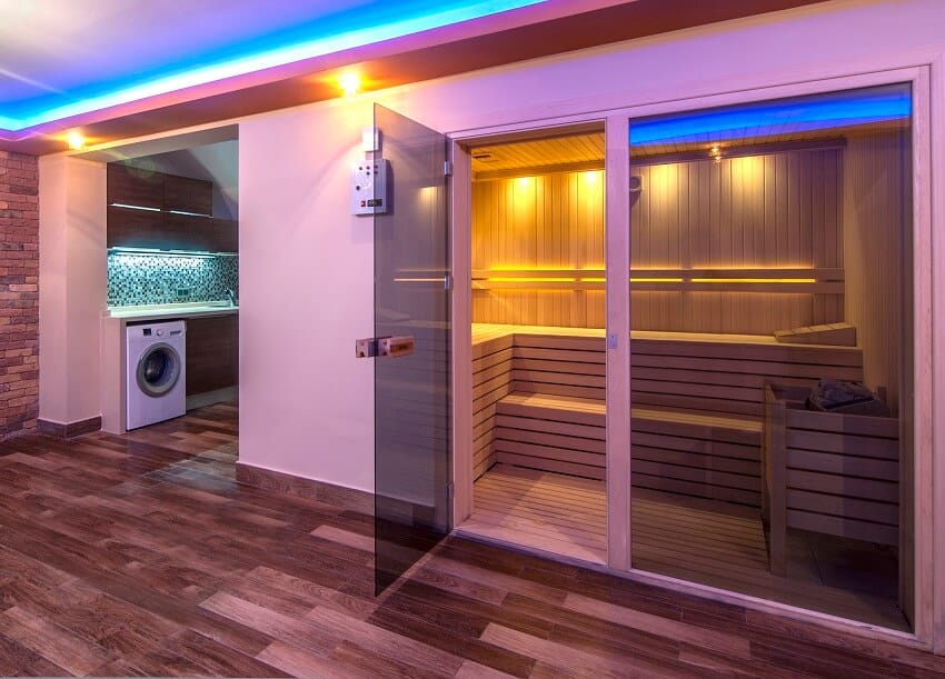 A room with brick wall wood tile floors laundry area and sauna enclosed in a glass with wood bench interiors and lighting fixtures