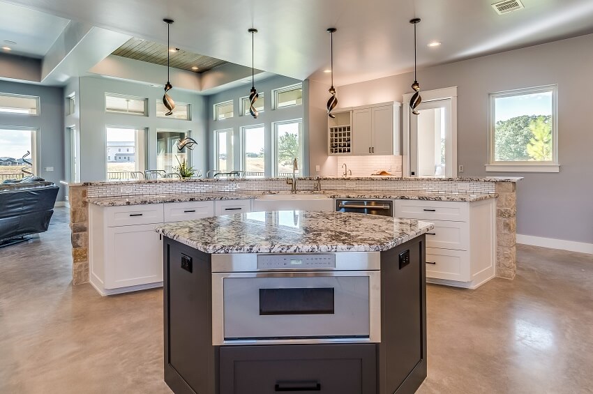 A smaller island with microwave drawer inside of a larger L-shaped island in an open kitchen with vinyl flooring quartz countertops and pendant lights