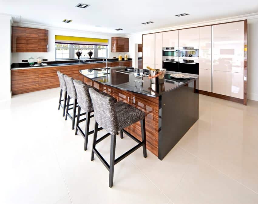 An off center kitchen island with a large black granite top, and four bar stools