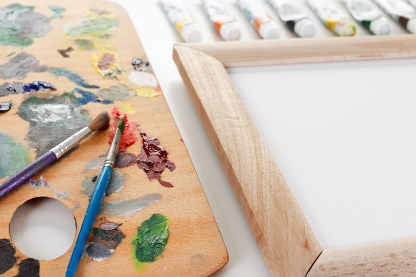 Art palette with paint, frame, and a brush on white background
