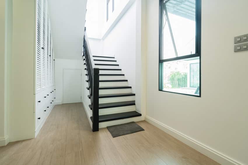 Stairs with black painted steps, railing, awning window, and wood flooring
