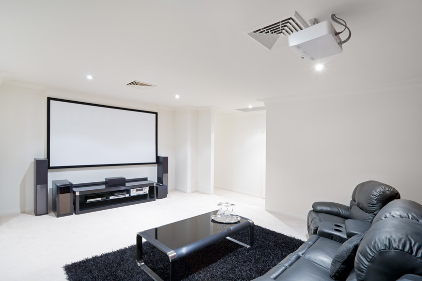 Basement with white painted floor, projector, and leather couch