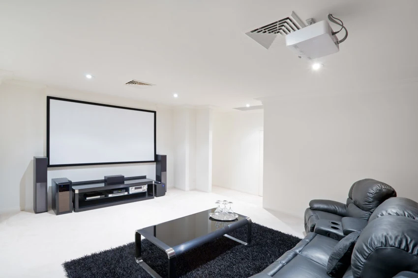 Basement with white painted floor, projector, leather couch, and recessed lights