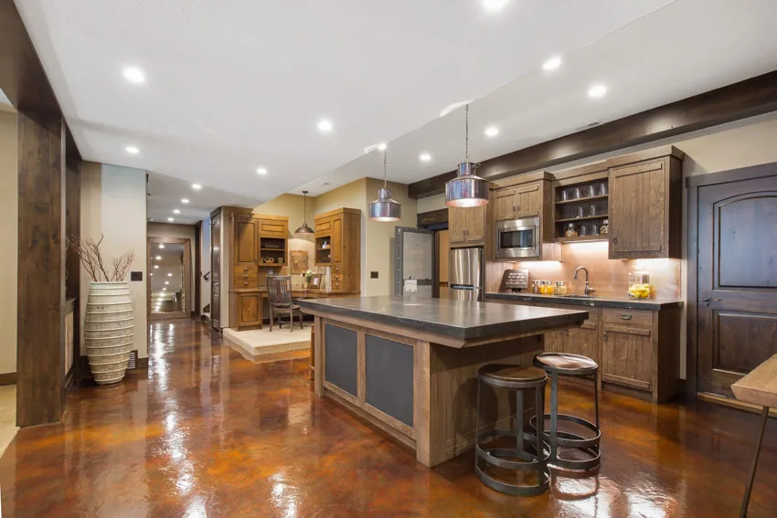 Basement kitchen with painted concrete floor, center island, wood cabinets, recessed lights, and stools