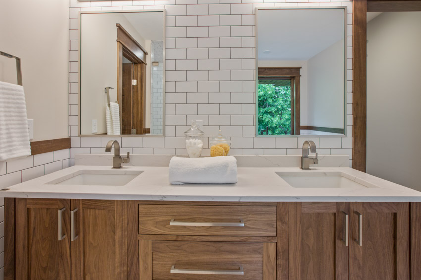 Bathroom vanity area with subway tile design, mirrors, sink, and wood cabinets