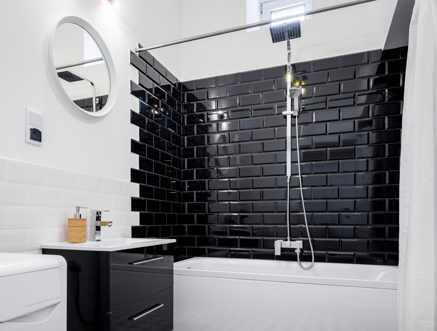 Bathroom with black tile shower wall, mirror, and tub