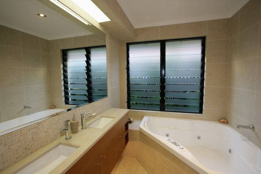 Bathroom with jalousie windows, mirror, sink, countertop, and tub