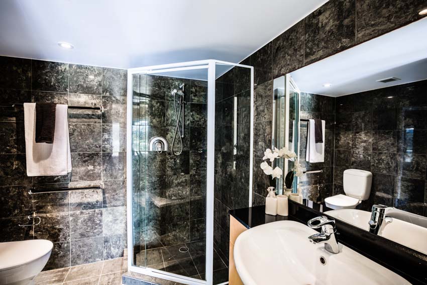 Bathroom with onyx shower wall, mirror, sink, towel bars, and toilet