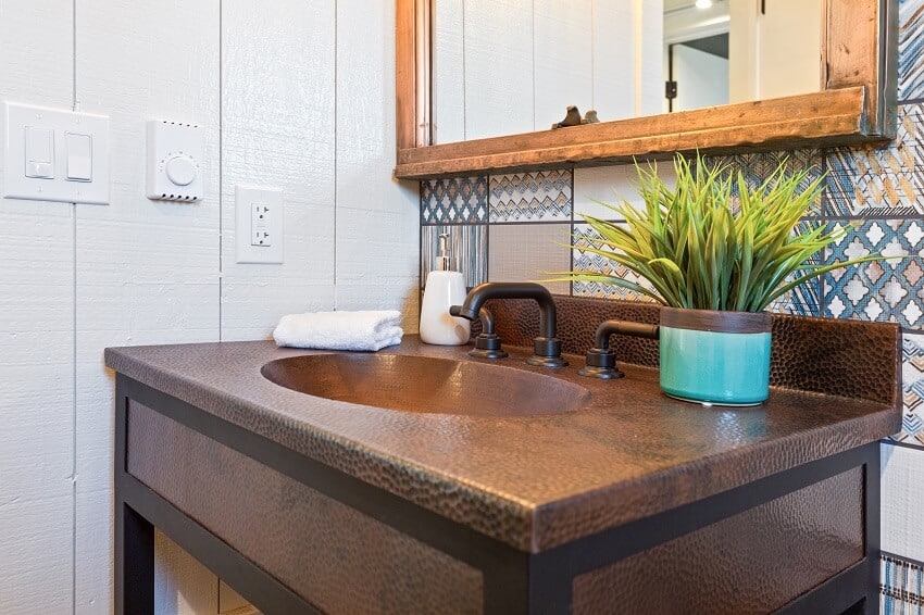 Bathroom with patterned tile wall mirror and copper countertop sink with a plant
