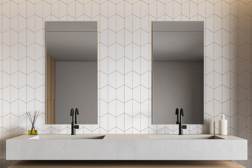 Bathroom with tile geometric backsplash, mirror, countertop, and faucets