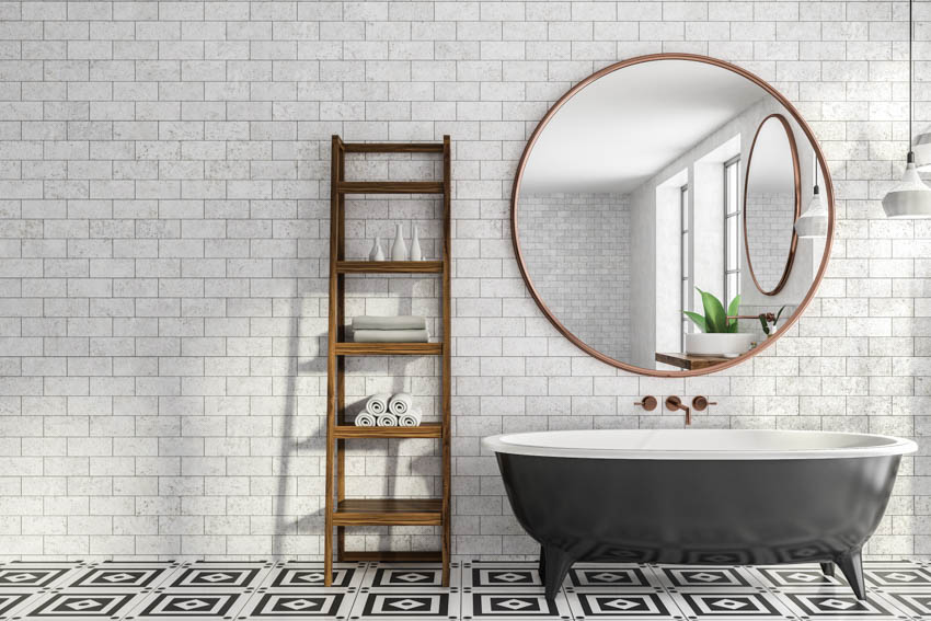 Bathroom with gray tile design, round mirror, and black tub