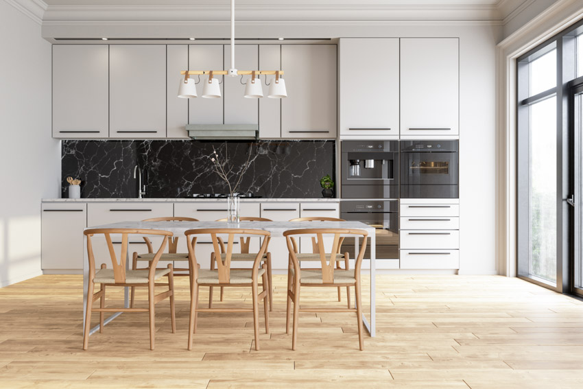 Beautiful kitchen with backsplash made of soapstone, chairs, white cabinets, and wood floor