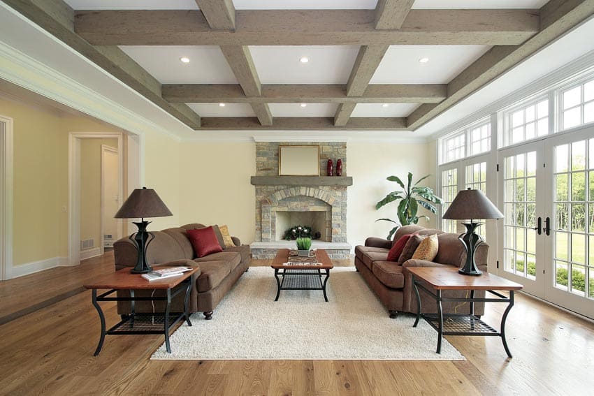 Beautiful living room with coffered wood ceiling, windows, couches, lamps, and a fireplace