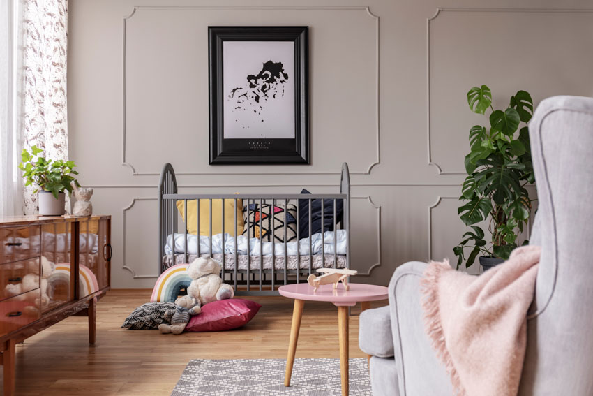 Beautiful nursery room with panel walls, crib, wood floor, sofa chair, windows, and indoor plants