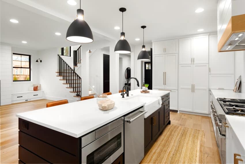 A beautiful white kitchen with with off center kitchen island and dark accents in new farmhouse style luxury home