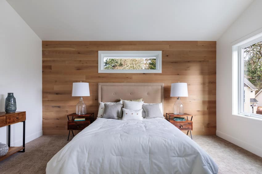 Bedroom with clerestory windows, wood accent wall, nightstands, lamps, and wooden floor