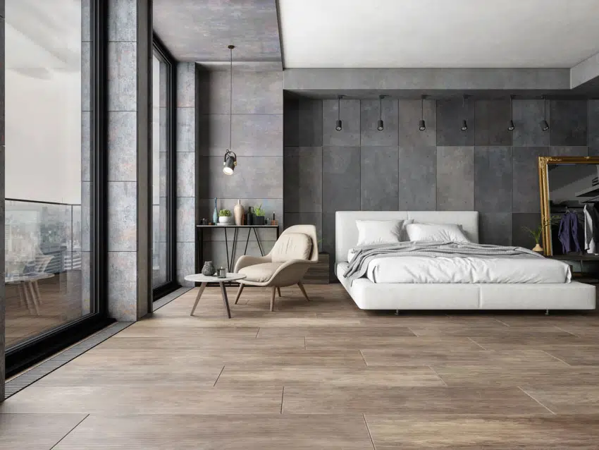 Bedroom with concrete wall, tall windows, bed, chair, and luxury vinyl floor tiles