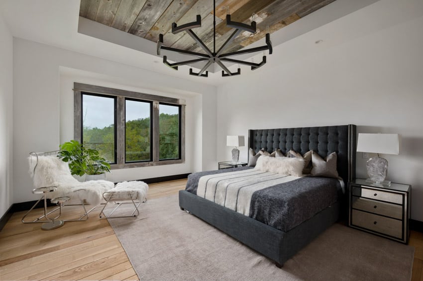 Bedroom with tray ceiling made of wood, bed, windows, carpet, nightstands, and lamps