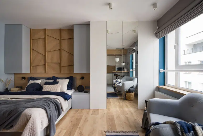 Bedroom with offwhite bed, blue pillows, Roman shades and tall mirror