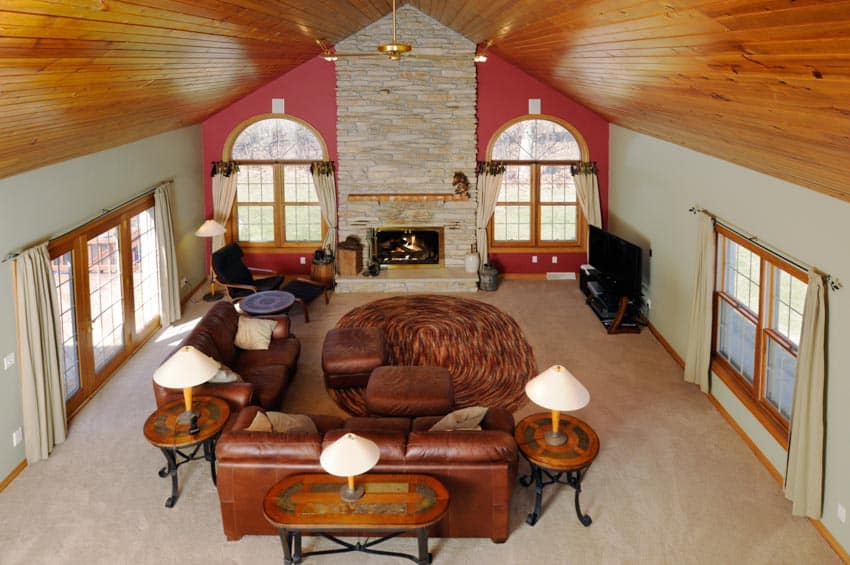 Big living room with leather couches, windows, and tongue and groove types of wood ceiling
