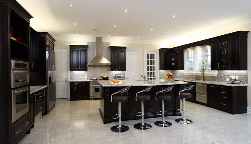 Black and white kitchen with tile flooring, oak cabinets, center island, high chairs, range hood, and countertop