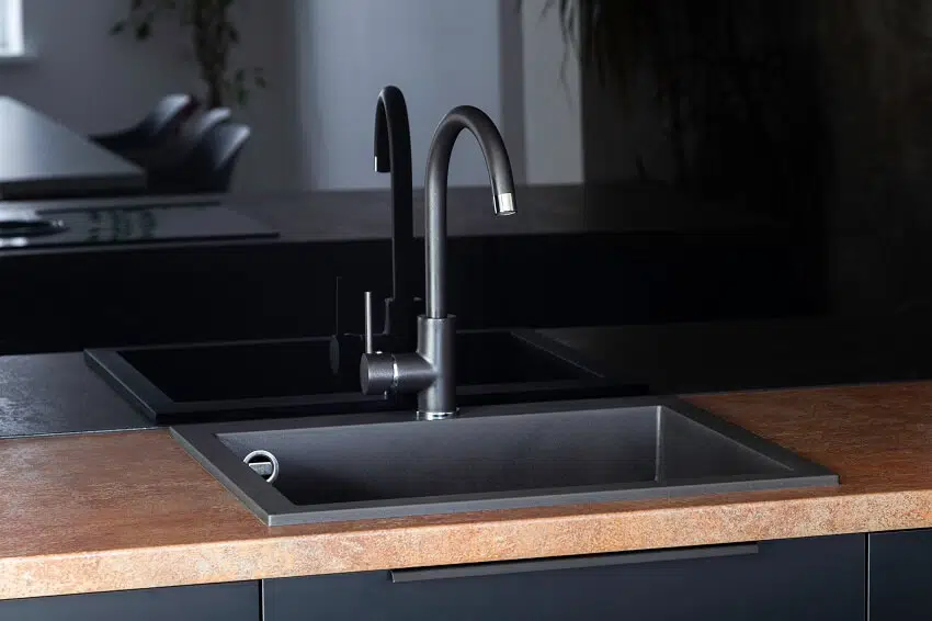 Black kitchen sink with a mixer black fronts black handles and black glossy backsplash with brushed copper countertop