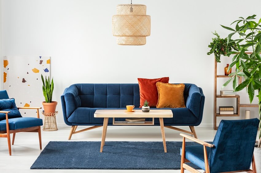 Blue wooden velvet sofa and armchairs in living room interior with plants coffee table on carpet rattan pendant lamp and wood shelves with book and decor