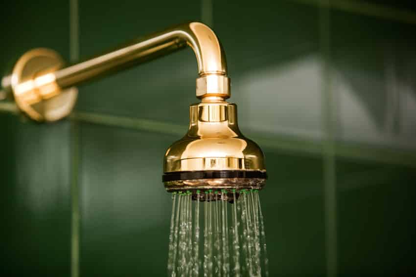 Brass gold shower head installed on green tile bathroom wall