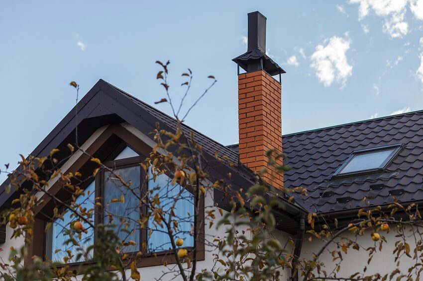 Brick chimney with metal chimney cap on a black metal roof with skylight window and dormer window