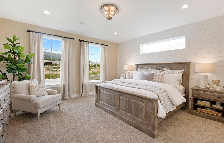 Bright guest room with white shiplap walls awning window above dark wood bed indoor plant armchair with throw pillow console table and the view of the mountains through large windows