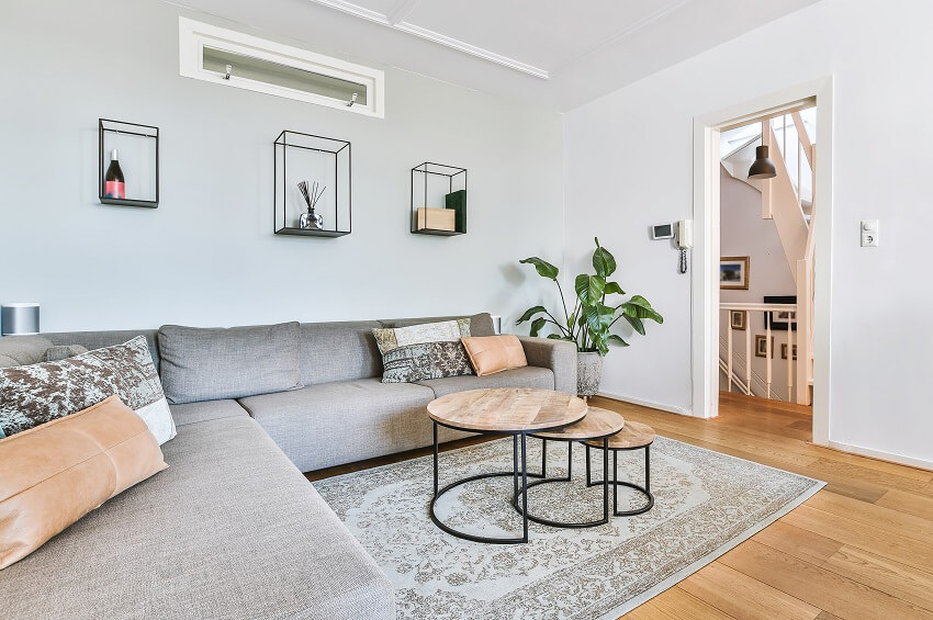 Room with large grey sofa, layered tables, wall decors and silk rug 