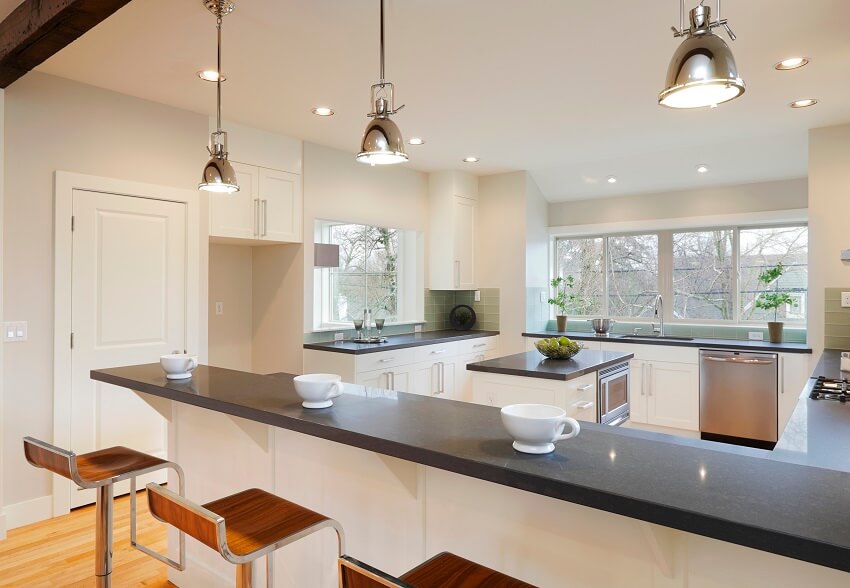 Bright luxury kitchen with green subway tile backsplash and a long breakfast counter with black top