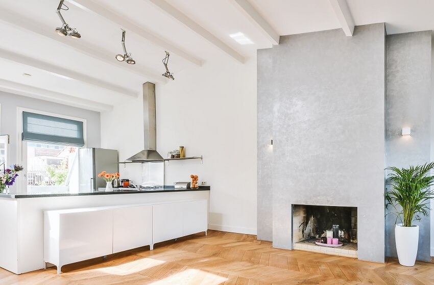 Bright open kitchen with ceiling beams track lighting granite countertops range hood parquet floor and candle in an old fireplace on grey wall