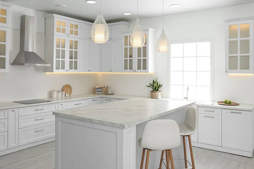 Bright white kitchen with panelled floor pendant lights ceramic cooktop range hood and kitchen island with honed granite countertop and stylish bar stools