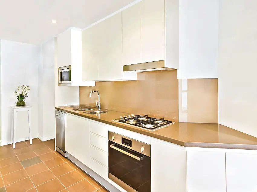 Bright white kitchen with tile floors stainless steel appliance and polished copper countertops and backsplash