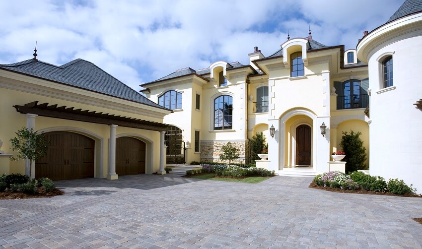 Bright yellow mansion exterior with columns stone pavers dark wood garage doors and shingle roofs with lightning rods